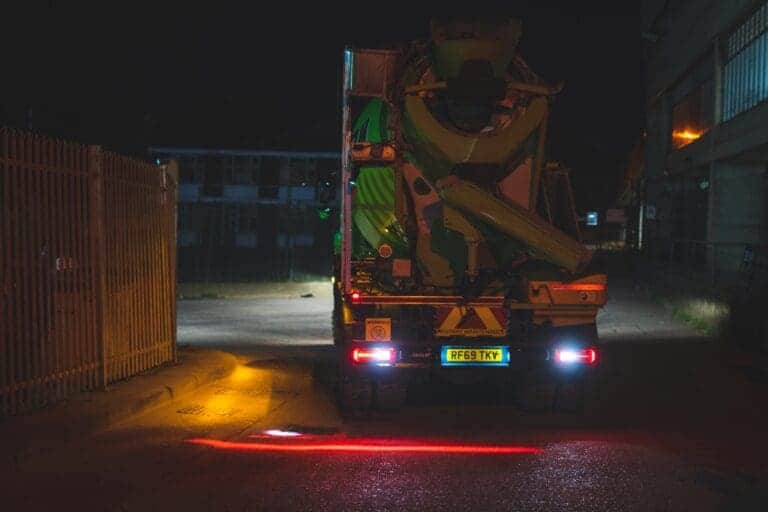 Rear view of a lorry at night using the FHOSS Cycle Lane system, projecting a red light onto the road to mark a safe exclusion zone for nearby cyclists.